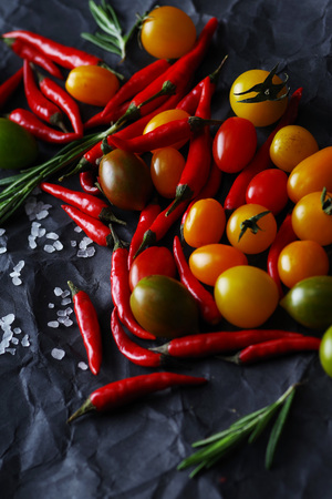 Multicolored piquant cherry tomatoes and chili peppers on a black background. Close-up.の写真素材