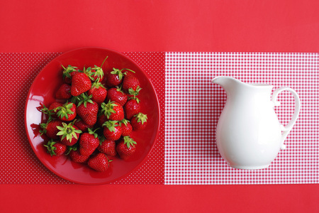 Bright red ripe summer strawberries and a white jug with cream on a red background. Top view.の写真素材