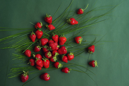 Brightly red natural ripe strawberry in the grass on a green background. Top view.