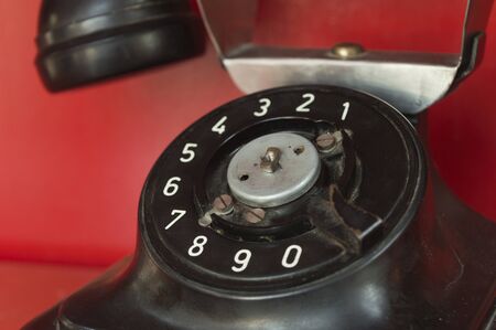 close up shot of black old style telephone set with rotary dial. Telephone stands on a shelf of red...