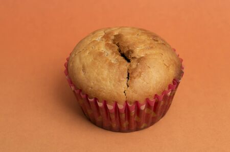 close up of fresh baked muffin in cupcake case over orange background
