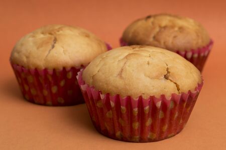 close up of three fresh baked muffins in cupcake cases over orange backgroundの写真素材