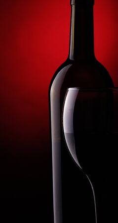 Still life with bottle and glass of red wine on a dark red background.の写真素材