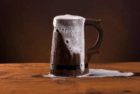 Wooden beer mug with foam on the dark redbackground の写真素材