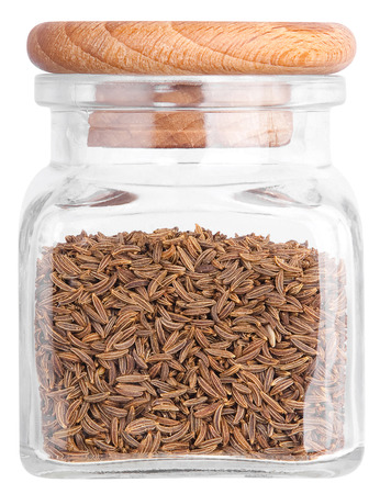 Cumin in a glass bottle with a wooden lid. Isolated on white background.の写真素材