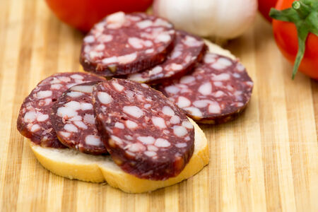 Two sandwiches with smoked sausage on wooden board, tomato and garlicの写真素材