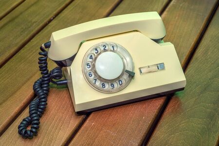 Old beige disk phone on wooden background