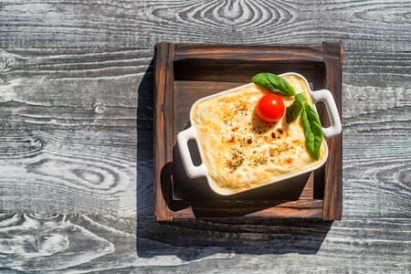 Tasty lasagna in baking dish on wooden board