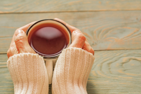 Woman in sweater holds cup of tea on wooden table