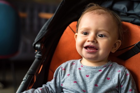 Happy baby girl sitting in modern stroller on walkの写真素材