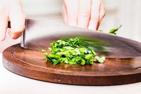 Female hands chopping herbs on wooden board