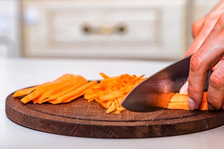 Womans hands slice carrot on wooden boardの写真素材