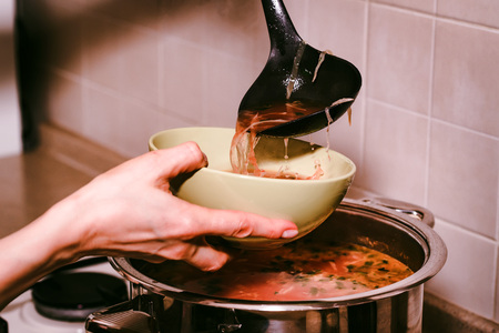 Hand pours borscht or red vegetable soup in bowl