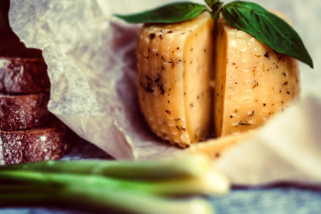 Rustic cheese with herbs on paper and vegetablesの写真素材