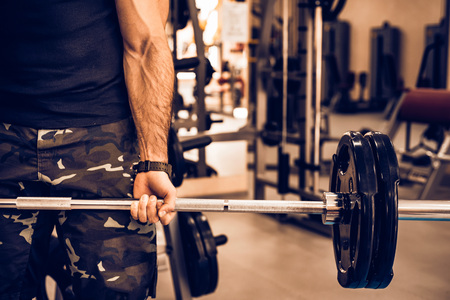 Sporty man holds barbell in gym closeの写真素材