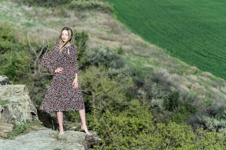 Beautiful girl in dress poses on rock in natureの写真素材