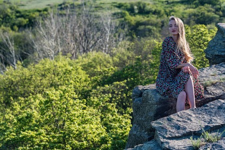 Beautiful girl in dress sits on rock in nature