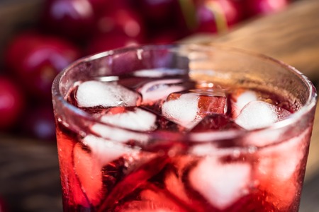 Close up fresh wild cherries, ice cubes and glass of cherry juice on dark background. Selective focus. Healthy food conceptの写真素材
