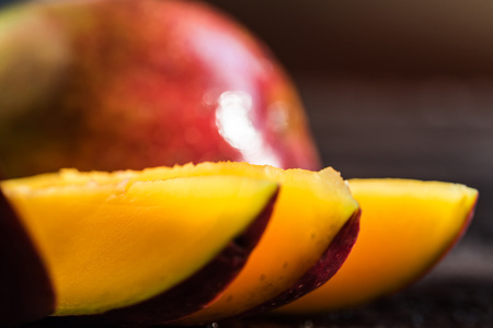 Whole and cut mango on a dark wood backgroundの写真素材