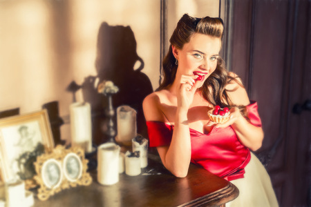 Pretty pin-up girl eats cake in retro interiorの写真素材