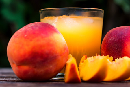 Glass of peach juice and peaches on wooden table