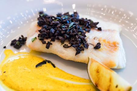 Pike perch fillet with vegetables and olives on white plate