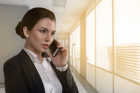 Portrait of serious pretty businesswoman talking on the phone in modern office