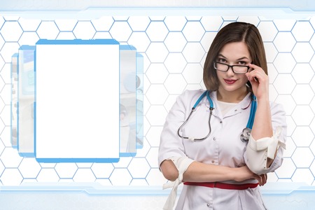 Young nurse or brunette doctor in white coat with stethoscope on hi-tech backの写真素材