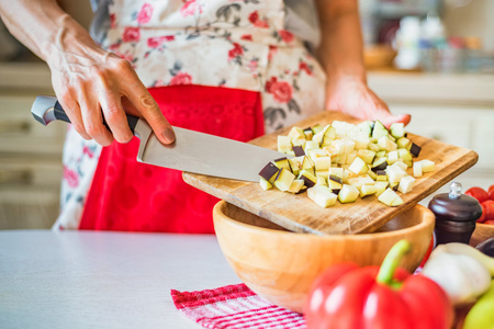 Female hand put cut eggplant in wooden bowl in kitchen. Cooking vegetables