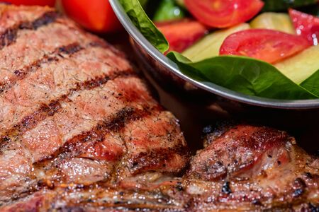 Close up freshly grilled bone steak on wood and fresh salad in bowlの写真素材
