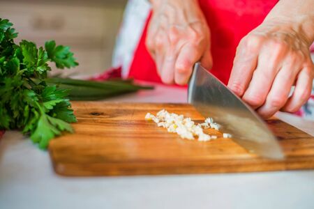 Female hand with knife chops garlic in kitchen. Cooking vegetables
