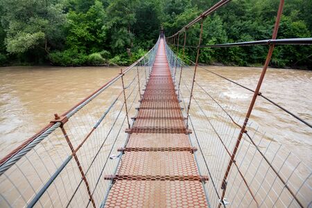 Narrow metal foot bridge across river in summerの写真素材
