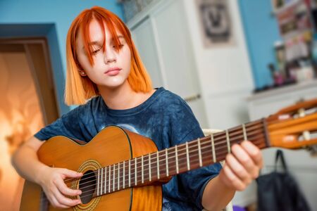 Pretty red-haired teenage girl plays guitar in her roomの写真素材