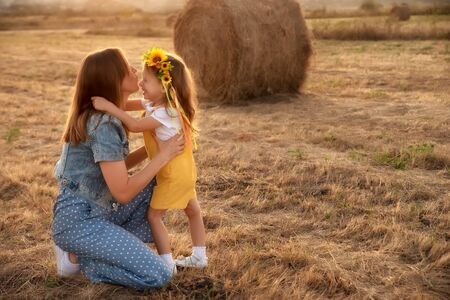 Happy girl child in yellow dress hugs young mom in autumn fieldの写真素材