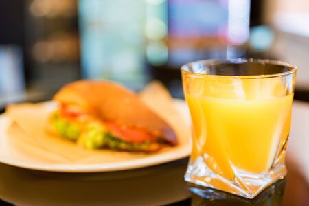 Fast food concept. Hot sandwich on plate and glass of orange juice close-up. Selective focusの写真素材