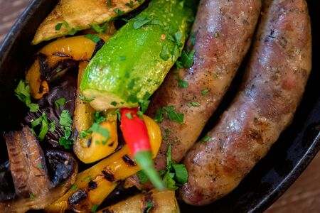 Grilled fried sausages kupaty on iron skillet grill with vegetablesの写真素材
