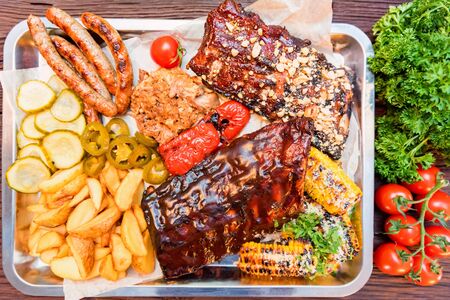Dish of mixed meats. Grilled ribs, chicken and sausages served with baked potatoの写真素材