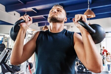Handsome strong man doing the exercises with kettlebells