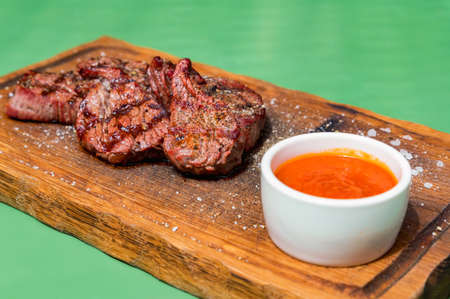 Grilled beef medallions served on a wooden kitchen board garnished with sauce