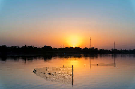 Stationary lift net fishing trap at river on sunset