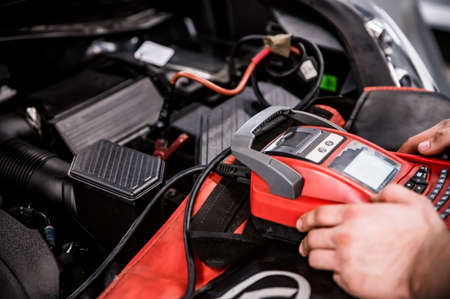 Hands of car mechanic checks auto battery chargeの写真素材