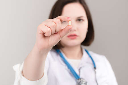 Portrait of young beautiful doctor shows drugs in hands on light backgroundの写真素材