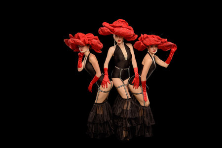 Three beautiful cabaret dancers in red hats isolated on blackの写真素材