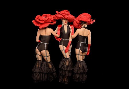 Three beautiful cabaret dancers in red hats isolated on blackの写真素材
