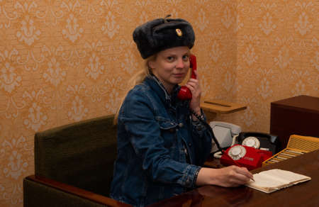 Woman rings from a Russian retro red telephone with a hat on her head, phone