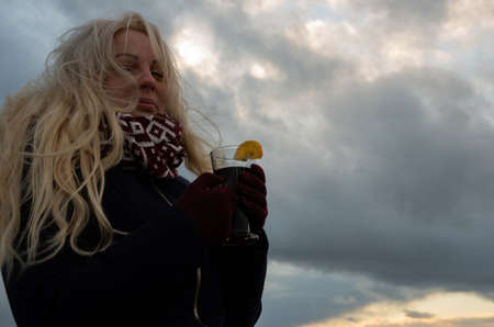 blonde woman sits by the sea and drinks a warm drink, autumn and couldの写真素材