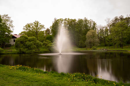 Fountain in a pond in the city, surrounded by trees and grass, chillの写真素材