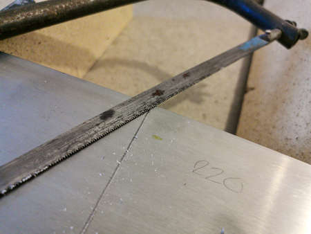 Rusty old hand saw blade cutting through aluminum plate during furniture restoration process at home with measurement value and pencil markingsの写真素材