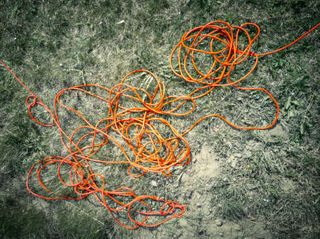 Dramatic high contrast random chaotic wire harness of bright red electricity extension cable on gray ground background in gardenの写真素材