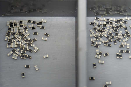 Abstract close-up of grey scattered microscopic 0402 SMT surface mount chip resistors power electronics components sorted in grey container background in random patternの写真素材